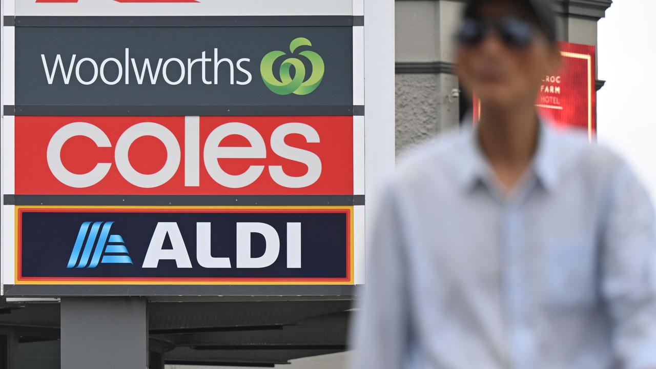 A man walks past signs of Woolworths, Coles and Aldi