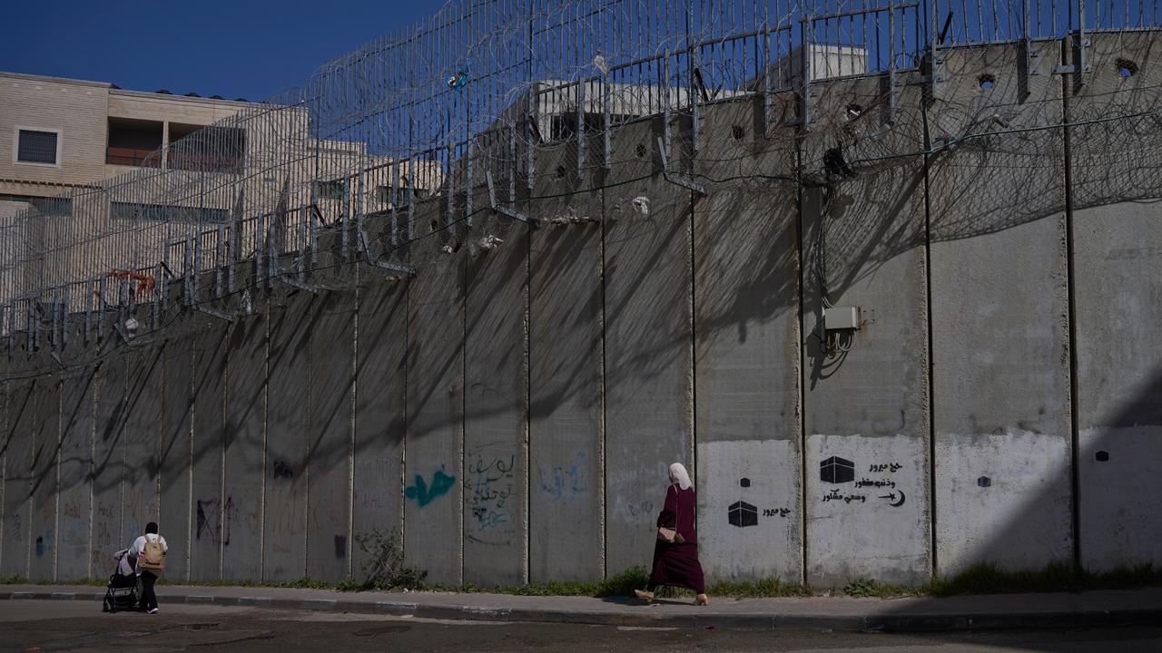 Palestinians walk along separation wall in West Bank