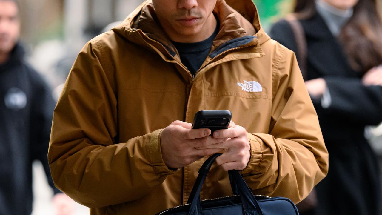 A person walks on the street while holding a phone